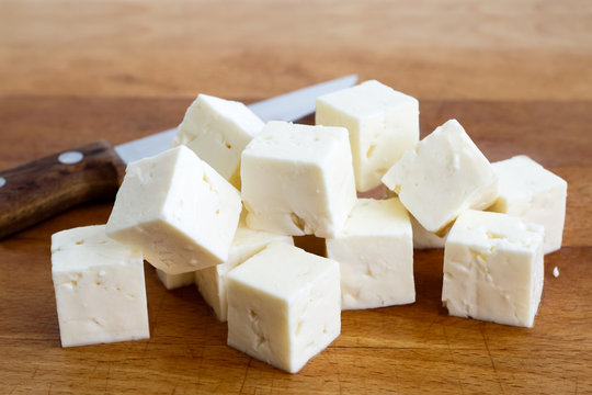 Square cubes of feta cheese isolated on wood board.