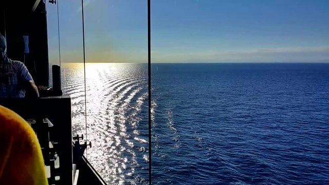 View Shining Waves of The Mediterranean Sea Through The Glass Wall of a Moving Cruise Ship. Cut Silhouettes of People and Furniture in The Foreground Emphasize The Depth of The Outer Space. 