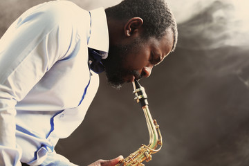 African American jazz musician playing the saxophone against smoky background