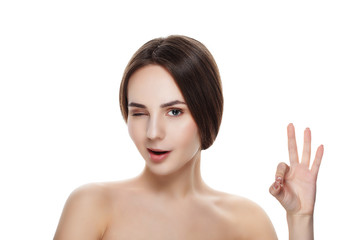 Fototapeta premium Pretty girl with natural makeup show gesture OKEY. Beautiful spa woman touching her face. Perfect fresh skin. Pure beauty model girl. Youth and skin care concept
