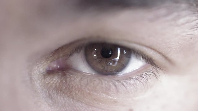 Big close up of a man's brown eye looking at the camera and looking around.  Desaturated colors, recorded in 4K at 60fps.