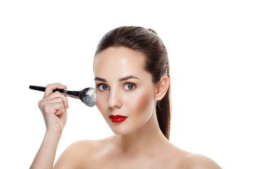 Fototapeta premium Beauty Girl with brush finish makeup apply highlighter. Bright Makeup for Brunette Woman with Beautiful Face. Makeover. Perfect Skin. Applying Make-up. Ideal for commercial 