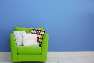 Fototapeta na wymiar Comfortable armchair with pillows against blue wall background