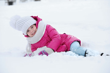 Fototapeta na wymiar Little girl with winter clothes lying on the snow outdoor