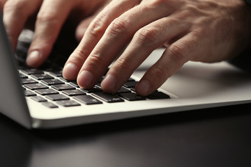 Male hands typing on laptop keyboard at table closeup