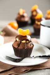 Tasty cupcake with slice of mandarin and chocolate on a plate over light wooden background