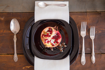 Half of pomegranate on a black plate lying on a festively decorated table on top view