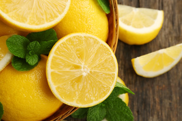 Fresh lemons with green leaves in bowl on wooden table closeup