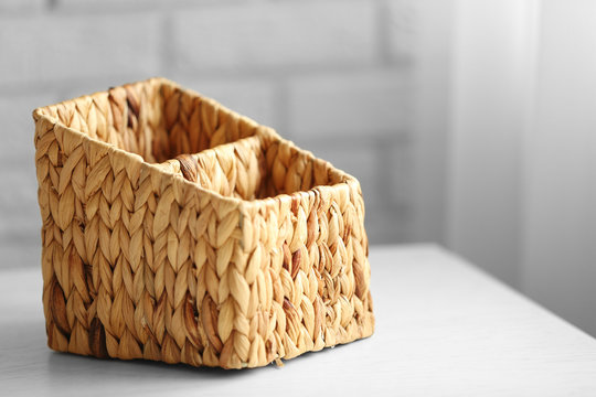 Wicker box on wooden table against brick wall background