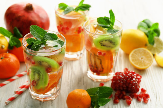 Refreshing cocktails with ice, mint, pomegranate seeds and slices of fruits on light wooden background