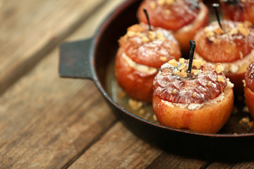 Baked apples with cottage cheese, raisins and walnut in pan on wooden table