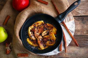 Sliced baked apple with star anise and cinnamon in a pan on wooden table