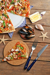 Sliced pizza with seafood, red pepper and olives on wooden table