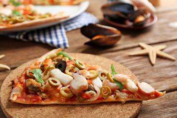 Pizza slice with seafood, red pepper and olives on wooden table