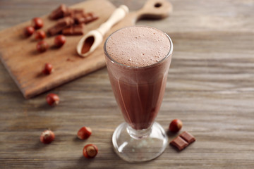 Glass of chocolate milkshake and nuts on wooden background