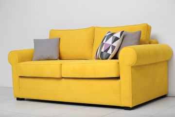 Yellow sofa with multicoloured pillows on white wall background
