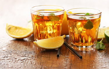 Two glasses of iced tea with lemon on wooden background