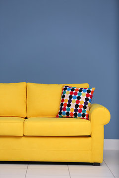 Yellow sofa and multicoloured pillow on a blue wall background