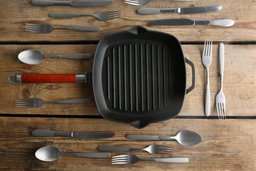 Grill pan and silver cutlery on wooden table, top view