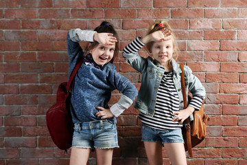 Obraz na płótnie Canvas Two stylish little girls with backpacks on wall background