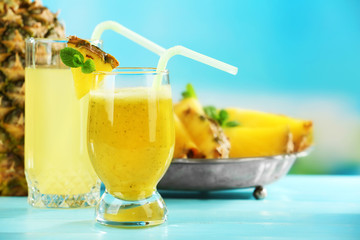 Pineapple juice and smoothie in cocktail glasses on blue background