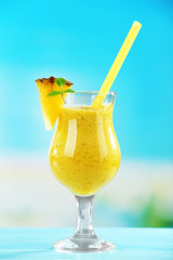Pineapple smoothie in cocktail glass with slices on blue blurred background