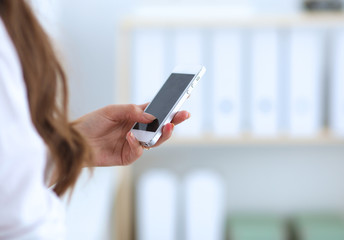 Businesswoman sending message with smartphone sitting in the office