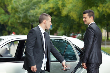 Young chauffeur is holding the door for the young businessman getting into the car