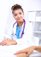 Beautiful young smiling female doctor sitting at the desk and writing.