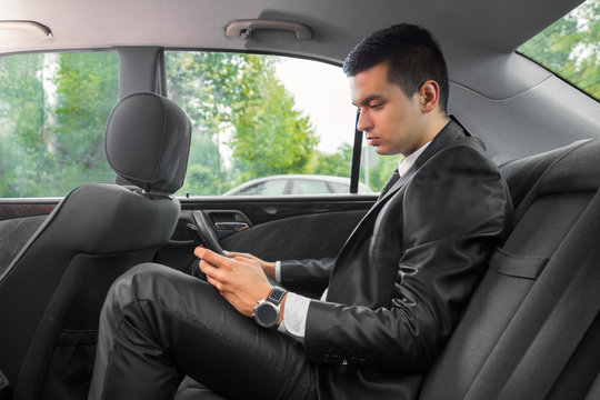 Young businessman using mobile phone while sitting on the back seat of the car