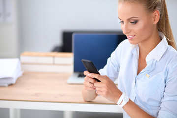 Businesswoman sending message with smartphone sitting in the office