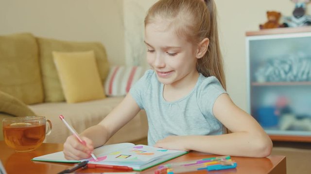 Girl 7 years old drawing in a notebook and smiling at camera