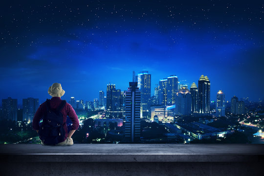 Traveler sitting on the rooftop watching city at night