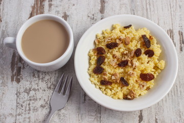 Cooked millet groats on white plate and cup of coffee with milk, healthy food and nutrition