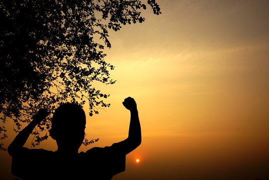 silhouette of a boy watching at sunset and raise up , happy enjoying moment, success concept