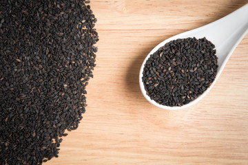 spoon of black sesame and a pile of black sesame on a wooden ba