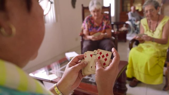 Old people in geriatric hospice: group of senior women playing cards and having fun together. The aged ladies sit on the sofa of the hospital and start a new match