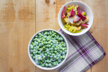 Frozen peas and bell pepper in bowl on wooden table
