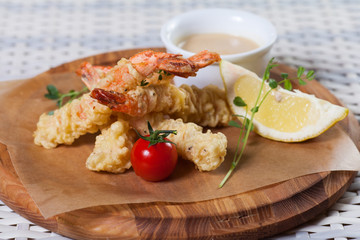 fried shrimp in batter, laid out on a board, with tomato, lemon, sauce and herbs