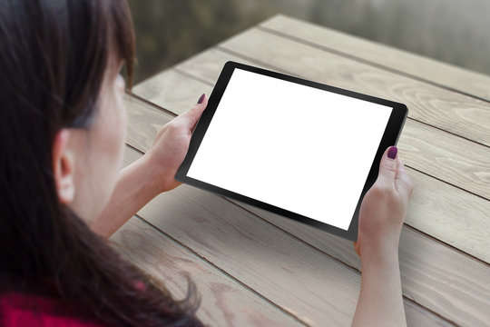 Black tablet with blank, white, isolated screen for mockup in woman hand. Table in background.