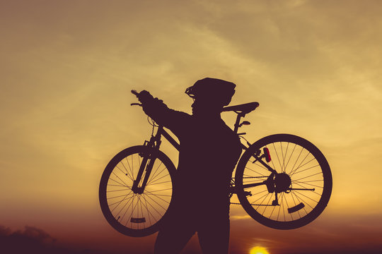 Healthy lifestyle. Silhouette of bicyclist carrying his bicycle