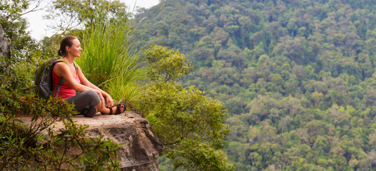 woman hiker sits on the edge of the cliff and enjoying tropical wood