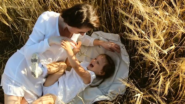 the daughter with the mother lying on the ground on the field with ears in the evening in summer