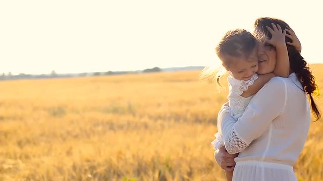 daughter hugging mother on field with ears in the evening in summer. slowmotion