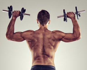 Rear view of a young male bodybuilder doing heavy weight exercise with dumbbells