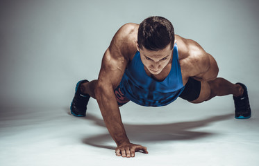 Strong young athlete doing push-ups on one hand. Sports concept - obrazy, fototapety, plakaty