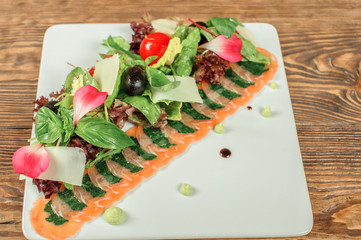 Delicious Appetizer Salmon Carpaccio sliced with cream and soy sauce decorated with leaves of arugula on a white plate isolated