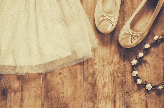 vintage chiffon girl's dress, floral tiara next to ballet shoes on wooden background. vintage filtered, sepia style image
