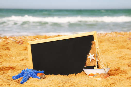 starfish, sailboat and chalkboard, on sea sand and ocean horizon
