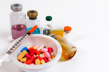 Many colored pills, capsules and syringe in a cup with a spoon and bottle of vaccine.